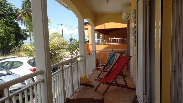 A balcony with a table and chairs, a red and yellow hammock, and a white car parked outside.