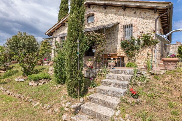 A stone house with a stone staircase leading to the entrance, surrounded by greenery and potted plants.