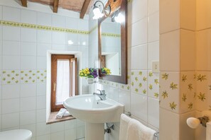 A bathroom with white tiles, a wooden door, a sink, a mirror, and a towel rack.