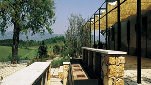 Un bâtiment moderne avec des piliers en pierre et une façade en verre donnant sur un paysage verdoyant.