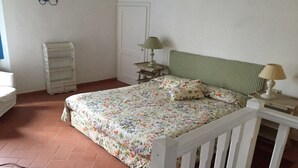 Une chambre à coucher avec une couvre-lit à motifs floraux, un berceau blanc, une table de chevet avec une lampe et une étagère fixée au mur.