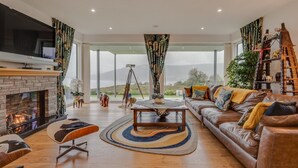 A modern living room with a fireplace, leather sofa, and a large window offering a view of the outdoors.