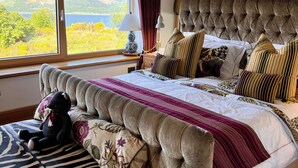 A bedroom with a large bed, a view of the outdoors, and wooden beams on the ceiling.