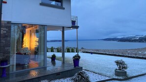 A modern house with a glass facade, a balcony, and a view of a body of water.