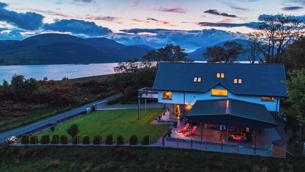 A modern house with a large deck, a swimming pool, and a view of a lake and mountains.