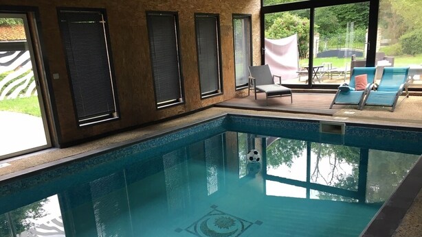 Une piscine intérieure dotée d’un sol carrelé, d’un motif décoratif au centre et offrant une vue sur l’extérieur grâce à de grandes fenêtres.