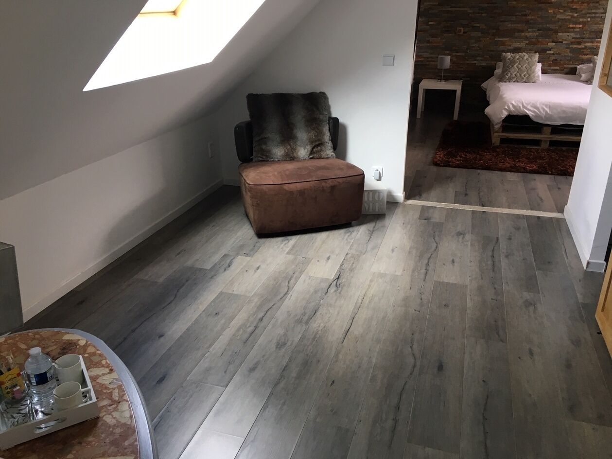 Um quarto no estilo loft com teto inclinado, uma poltrona de couro marrom, uma cama com edredom branco e uma pequena mesa de cabeceira.