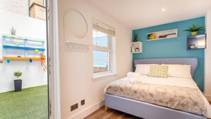 A bedroom with a bed, a window, a wall-mounted shelf, and a view of a garden. - M02A - Modern 2Bed patio apartment in Hyde Park (London)