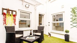 A patio with wicker furniture, a bottle of wine, and a newspaper on a table. - M02A - Modern 2Bed patio apartment in Hyde Park (London)