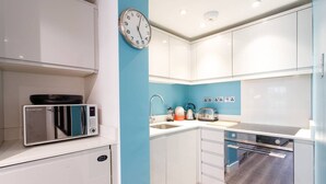 A compact kitchen with white cabinets, a microwave, a kettle, and a toaster. - M02A - Modern 2Bed patio apartment in Hyde Park (London)