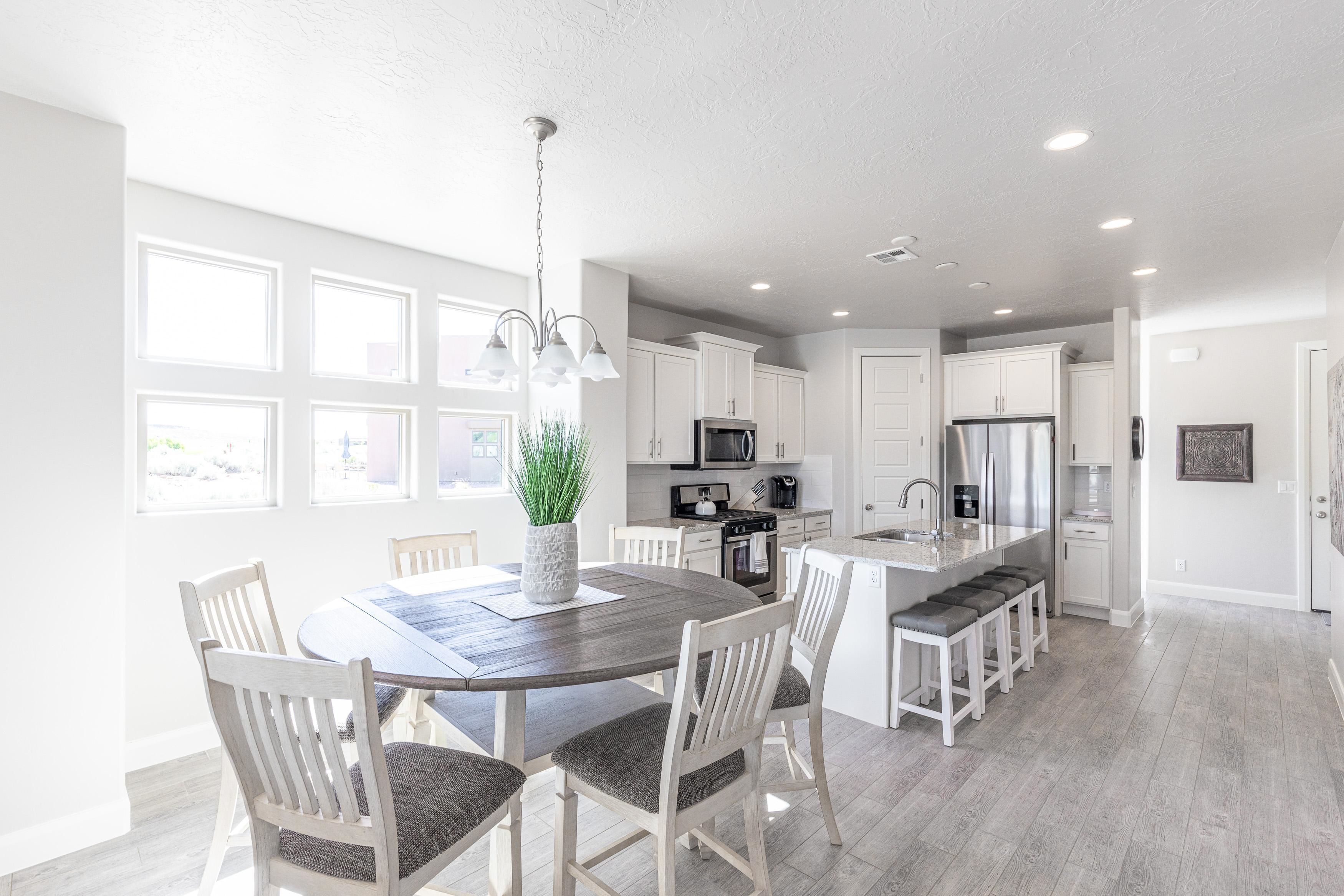 A modern kitchen with white cabinets, a central island, and a dining area with a wooden table and chairs.