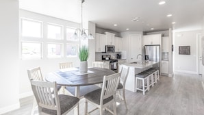 A modern kitchen with white cabinets, a central island, and a dining area with a wooden table and chairs.