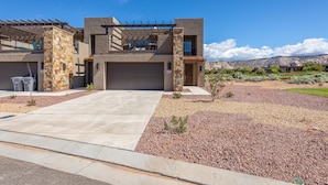A modern two-story house with a stone facade, a covered patio, and a view of the desert landscape.