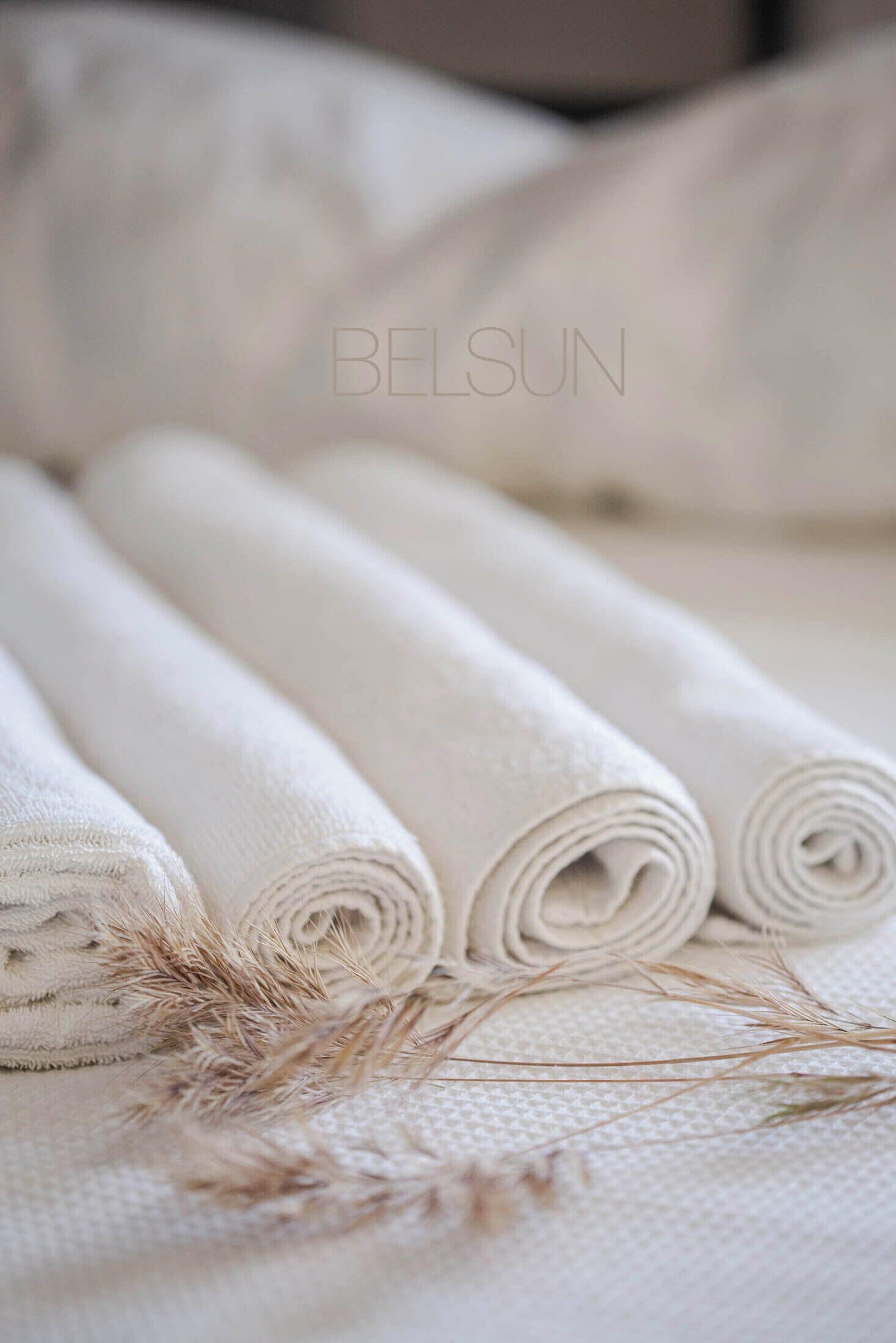 Een bed met gerolde witte lakens en gedroogde korenbloemen.