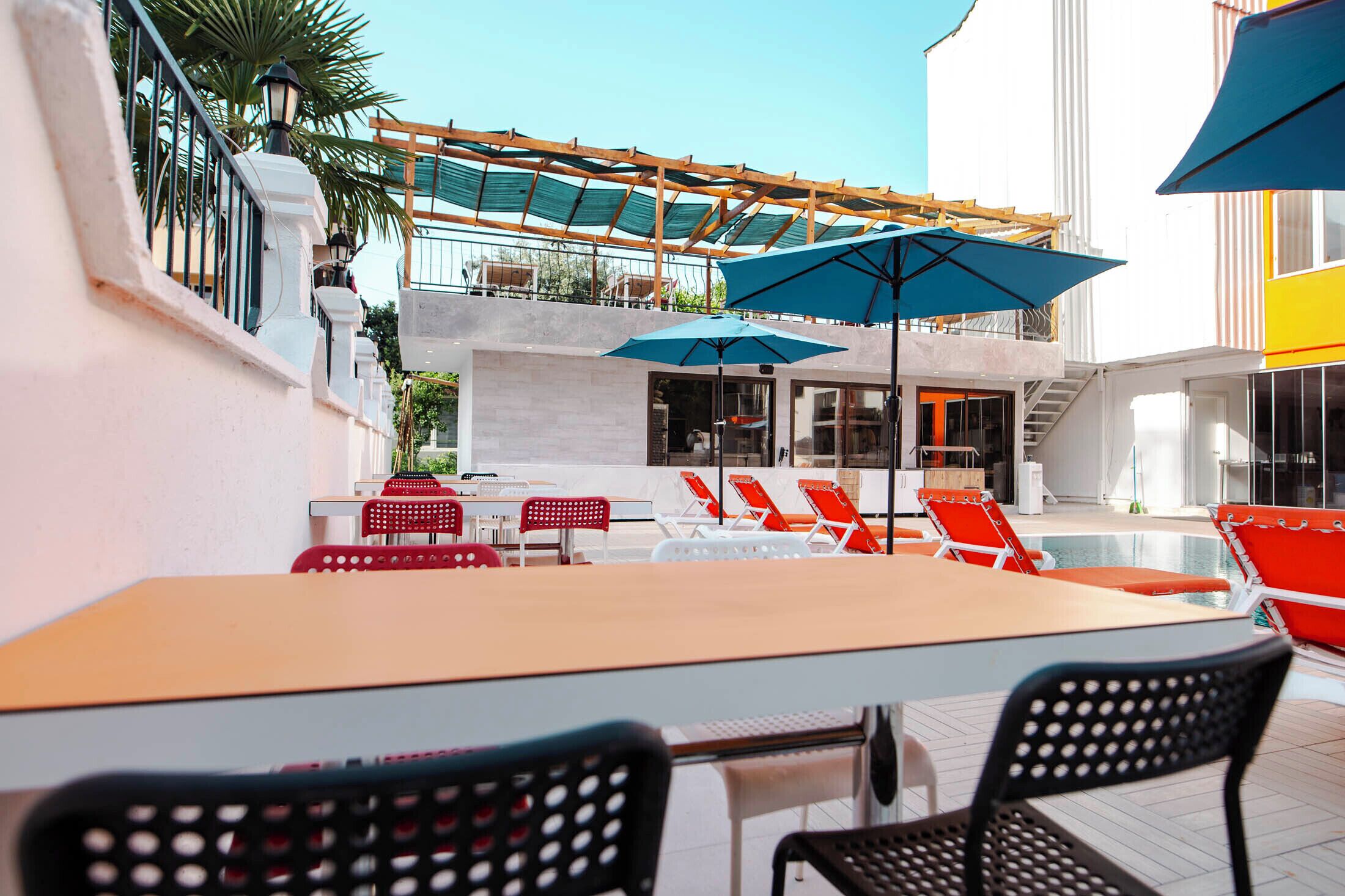 A rooftop pool area with lounge chairs and umbrellas, a covered seating area, and a staircase leading to an upper level.
