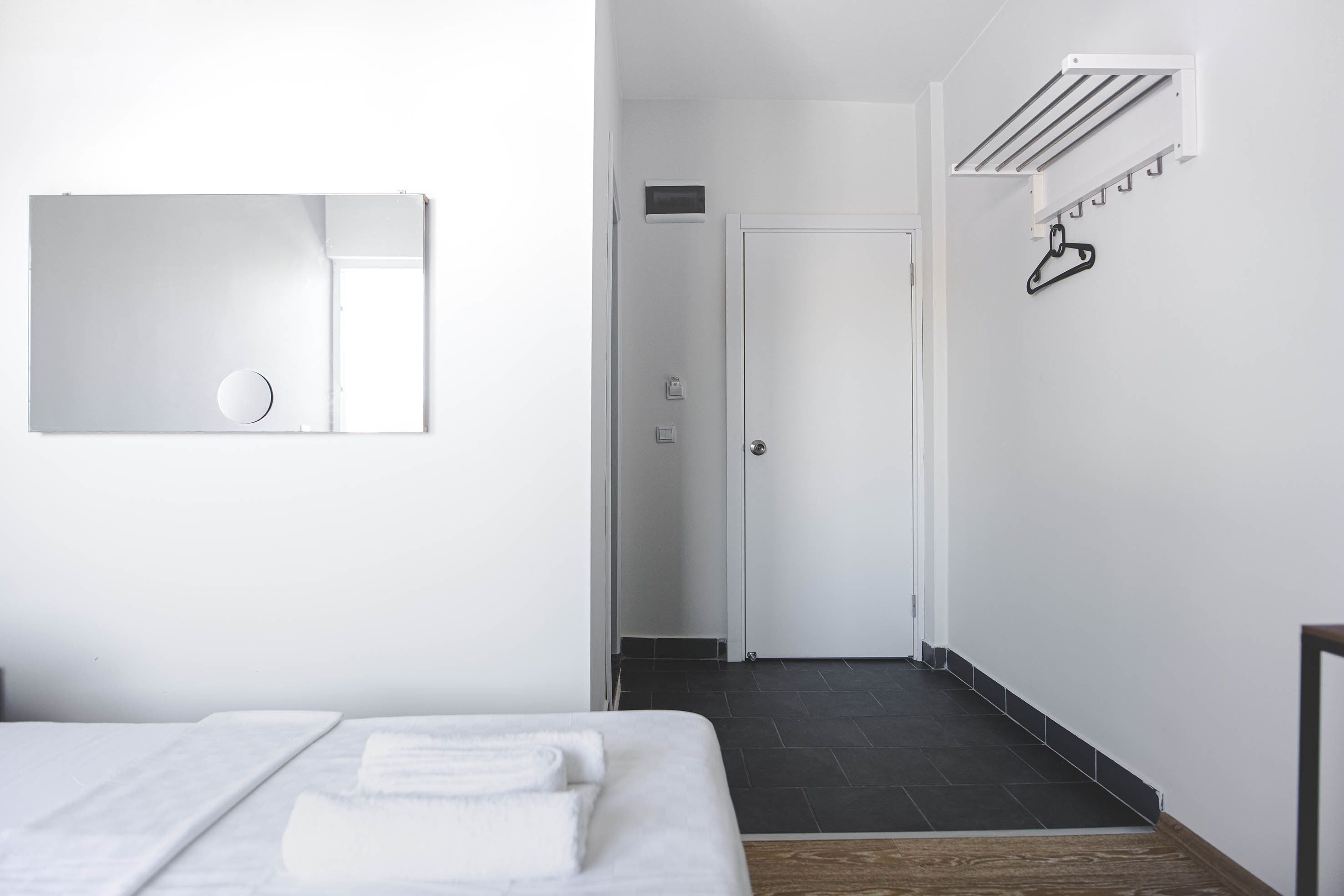 A modern hotel room with a bed, a mirror, a door, and a wall-mounted drying rack.
