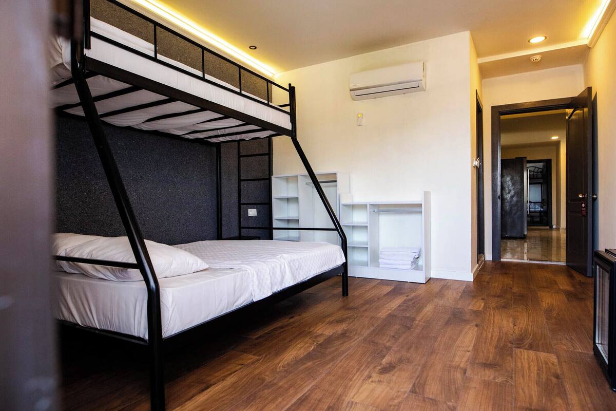 Une chambre avec un lit superposé, un plancher en bois, des murs blancs et une armoire intégrée.