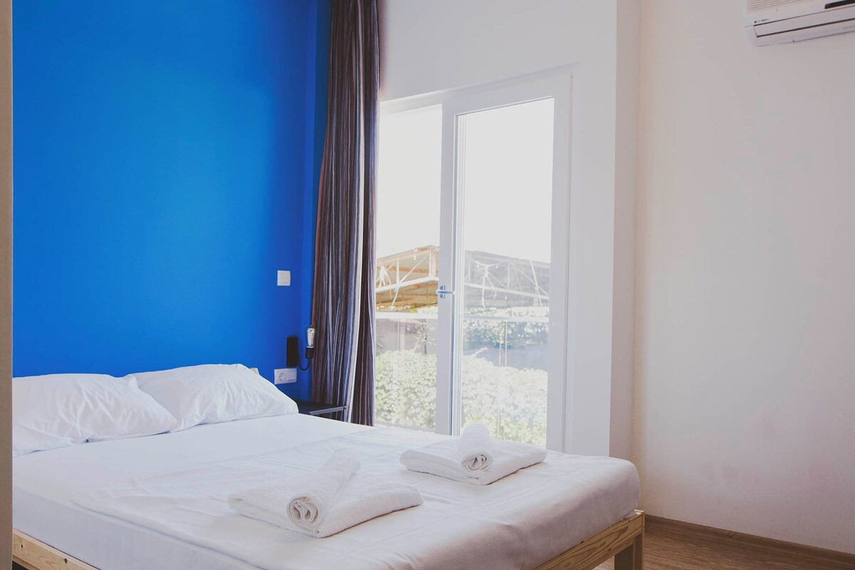 Une chambre à coucher avec un lit en bois, un mur bleu, une fenêtre avec des rideaux et un appareil de climatisation.