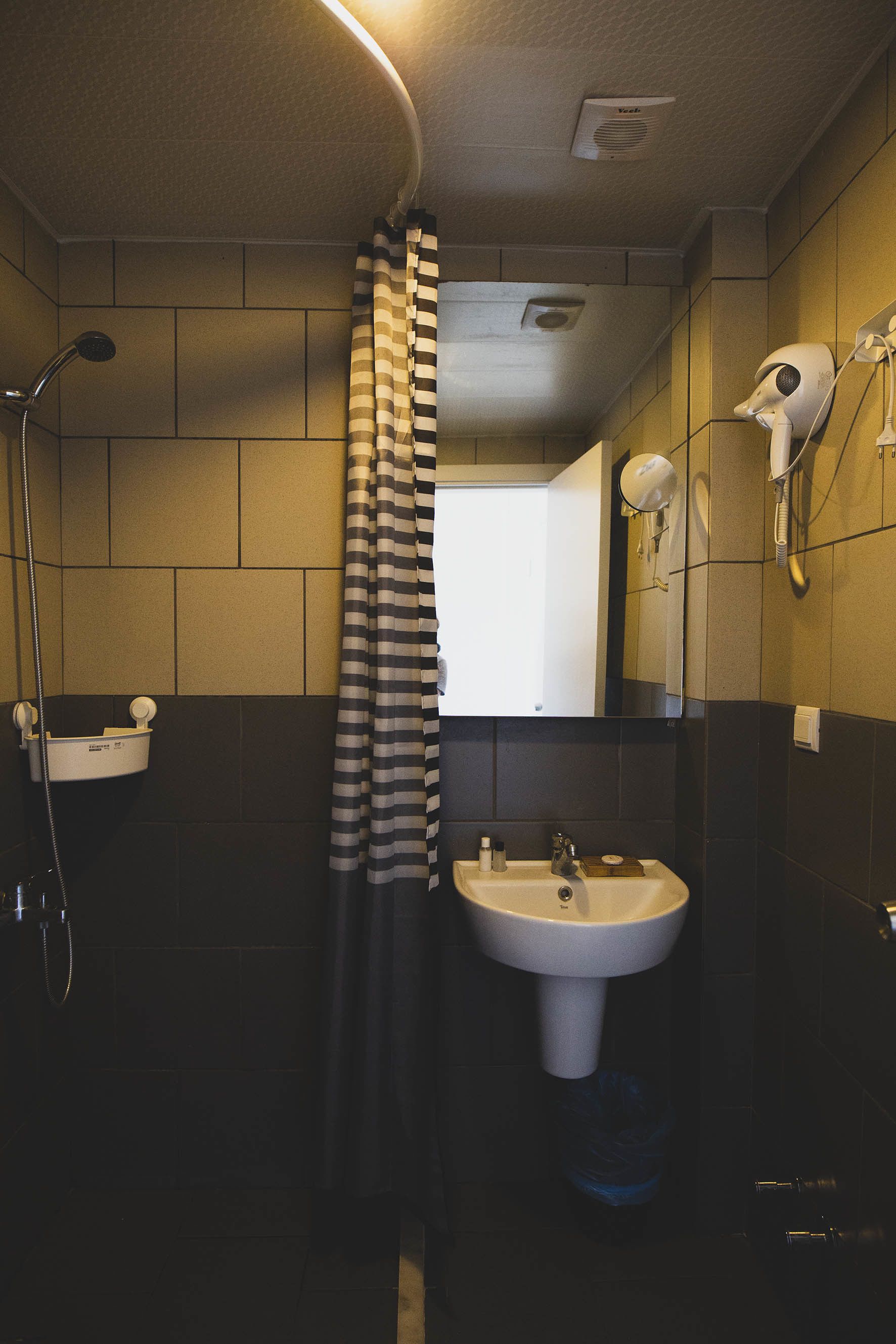 A bathroom with a shower, a sink, and a hairdryer mounted on the wall.