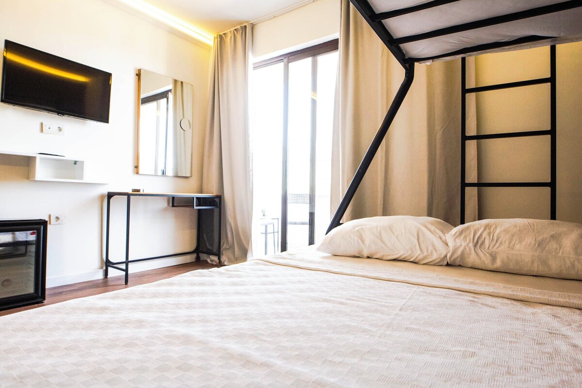 Een slaapkamer met een bed, een aan de muur bevestigde televisie, een bureau en een raam met gordijnen.