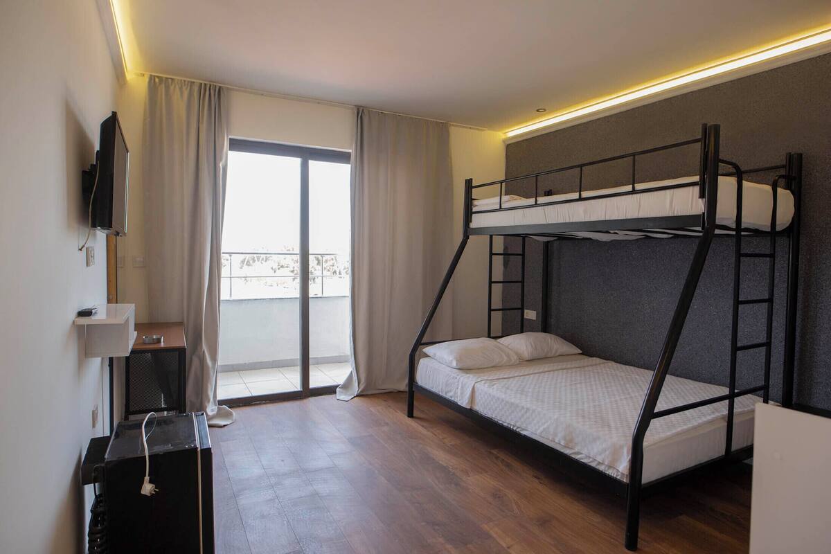 Une chambre avec un lit superposé, une télévision, un bureau et une fenêtre avec des rideaux.