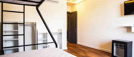 Un dormitorio con cama, armario empotrado, refrigerador negro pequeño y televisor montado en la pared.