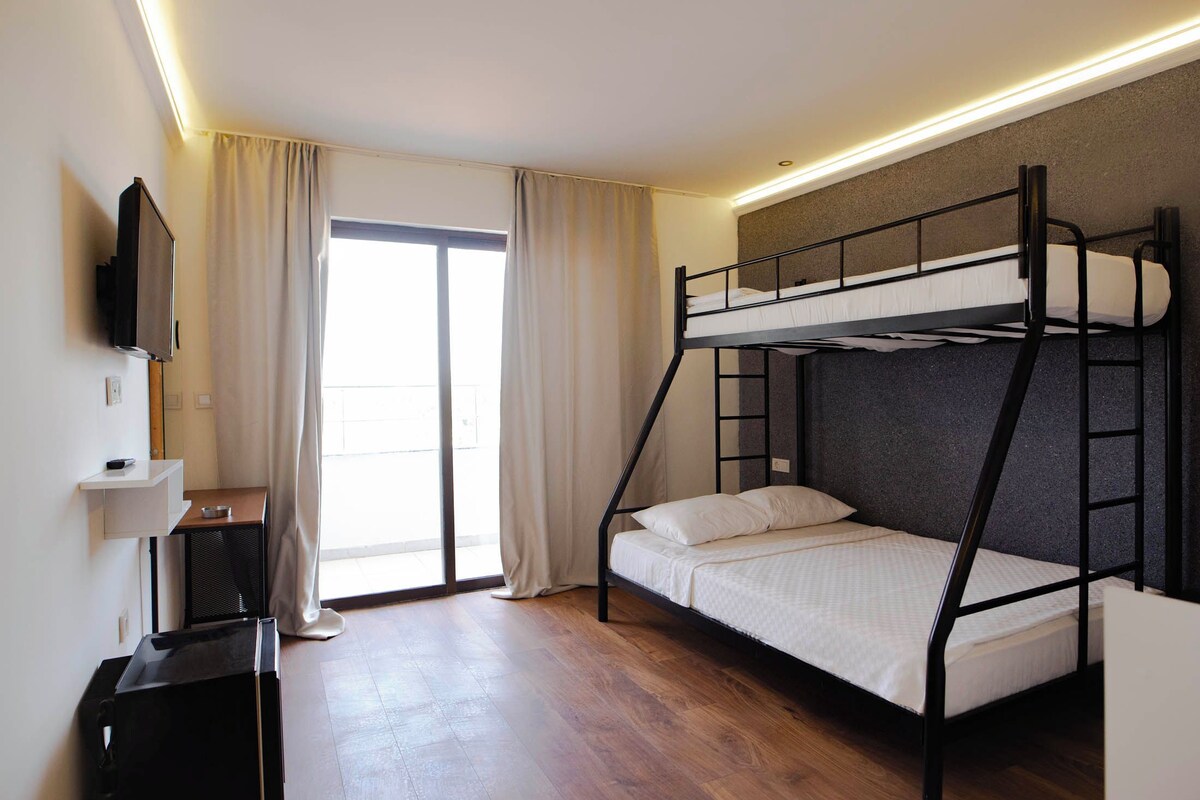 A bunk bed room with a television, a small table, and a sliding door to the outside.