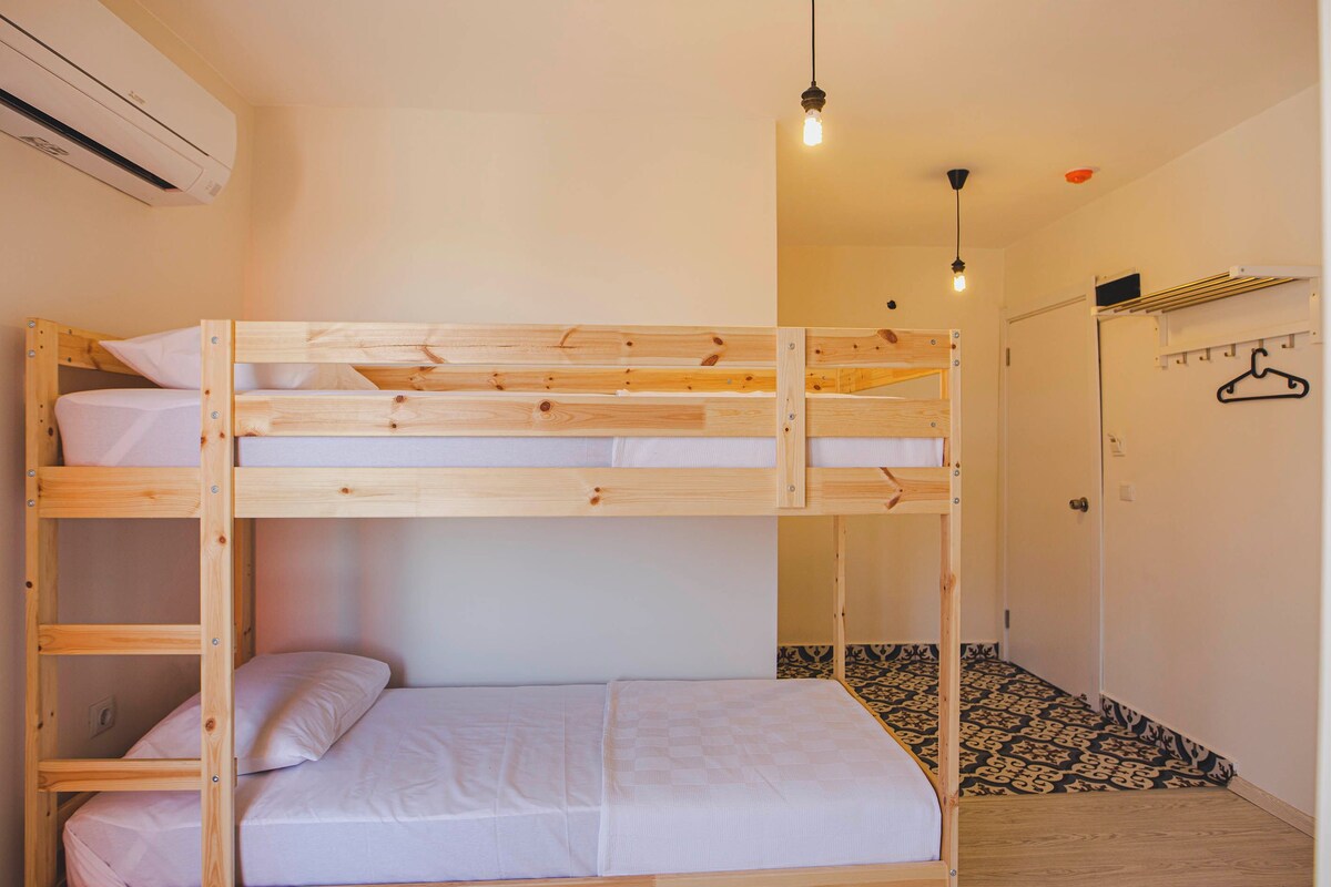 Un lit superposé avec une structure en bois et une literie blanche, un luminaire suspendu et un sol à motifs.