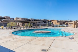 A swimming pool with a circular hot tub in the center, surrounded by lounge chairs and a covered area.