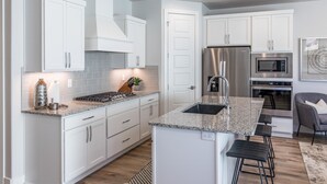 A modern kitchen with white cabinets, granite countertops, stainless steel appliances, and a bar area with stools. - Desert Solace (St. George)