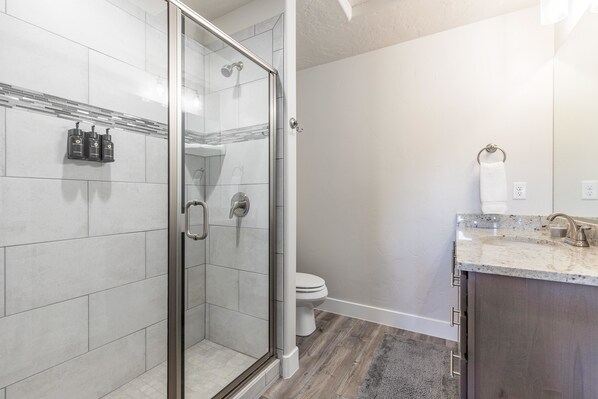 A modern bathroom with a glass-enclosed shower, a toilet, and a vanity with a sink and countertop.