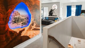 Un salón con un mural grande en la pared, un telescopio y un sofá con cojines.