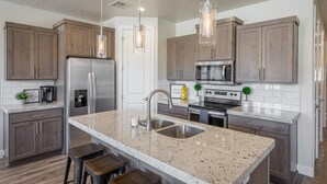 Una cocina moderna con encimeras de granito, electrodomésticos de acero inoxidable, armarios de madera e iluminación colgante.