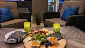 Cómoda zona de estar al aire libre con mobiliario de mimbre y cojines estampados con motivos de estrellas, una mesa con una tabla de quesos, frutas y velas.