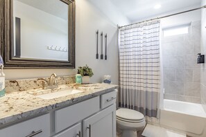 Un baño con lavamanos de mármol, inodoro, bañera y cortina de ducha.