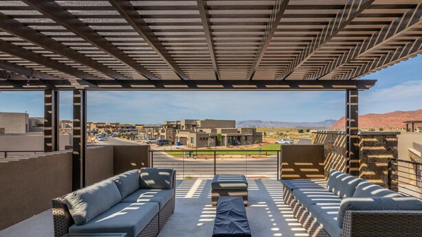 A covered outdoor seating area with wicker furniture and a view of a cityscape. - Fable House (St. George)