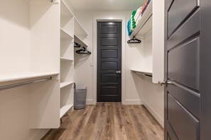 A narrow hallway with white walls, a black door, and wooden flooring. Shelves and hooks are mounted on the walls. - Fable House (St. George)