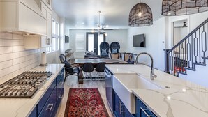 A modern kitchen with a central island, built-in appliances, and a dining area with a red patterned rug. - Fable House (St. George)