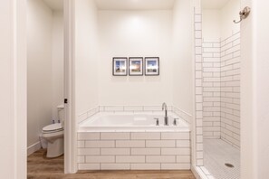 A bathroom with a white bathtub, a toilet, and a shower area with white tiles. - Fable House (St. George)