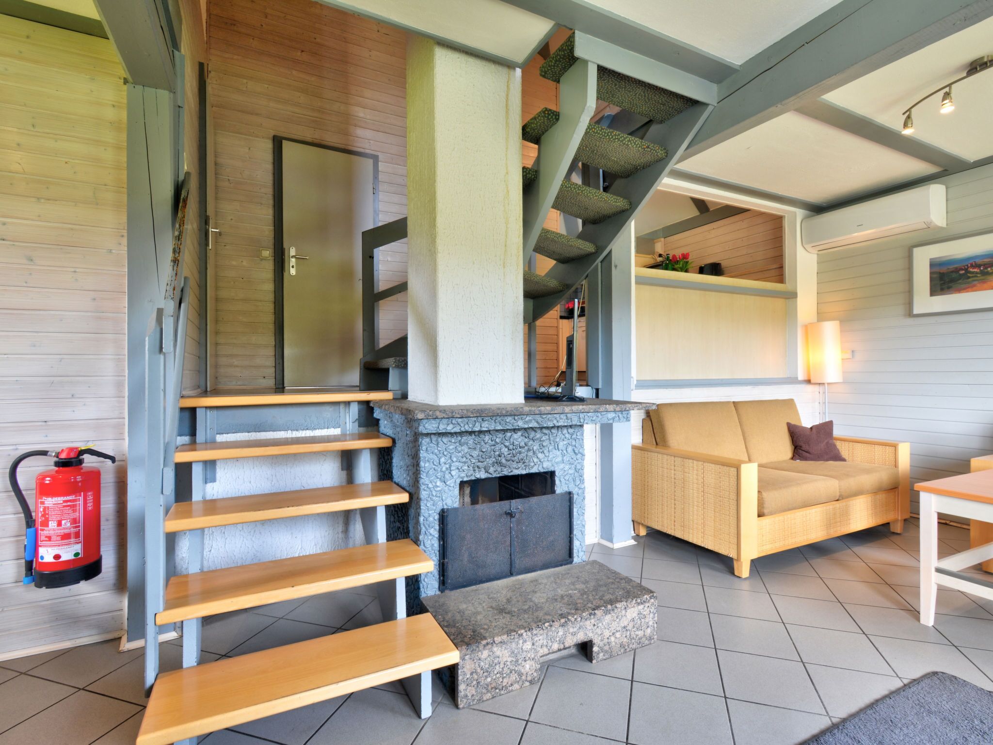 A modern interior with a stone fireplace, wooden staircase, and a cozy seating area.