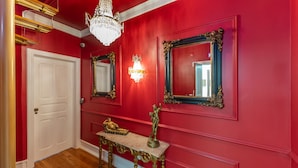 A hallway with red walls, a white door, and a marble console table with a statue. - Modern stylish studio in downtown Lisbon center - new to Vrbo (Lisboa)