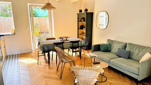 Ein gemütliches Wohnzimmer mit einem grünen Sofa, einem Korbstuhl und einem Essbereich mit Tisch und Stühlen.