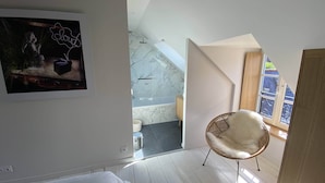 Ein modernes Badezimmer mit einer Duschkabine aus Glas, einer Wand mit Marmorfliesen und einem Holzstuhl am Fenster.
