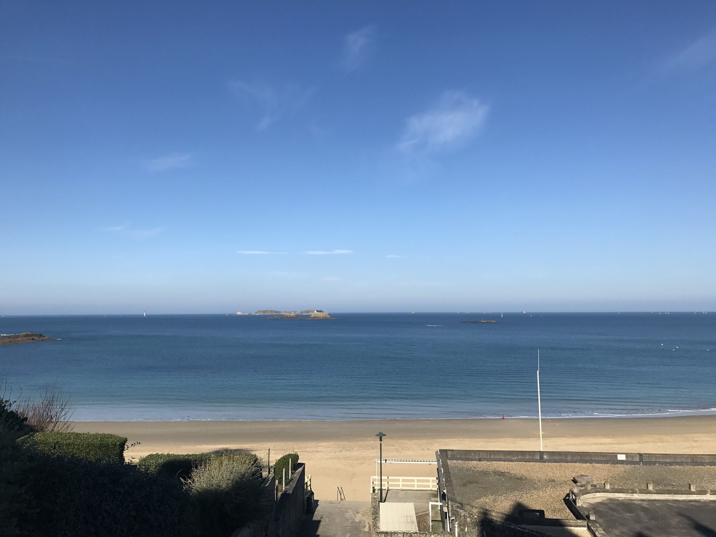 A coastal view with a sandy beach, a clear blue sky, and distant islands.