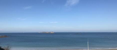 A coastal view with a sandy beach, a clear blue sky, and distant islands.