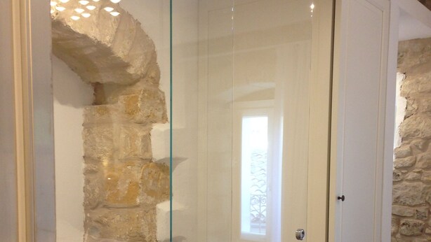 A room with a glass door leading to a bathroom, stone walls, and a small window. - Casa San Pietro Modica (Modica)