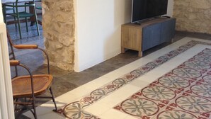 A room with stone walls, a flat-screen TV on a wooden stand, a patterned rug, and a chair. - Casa San Pietro Modica (Modica)