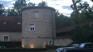 A stone tower with a small window, a gravel driveway, and a parked vintage car. - Standard double room "B" (Bruyères-et-Montbérault)