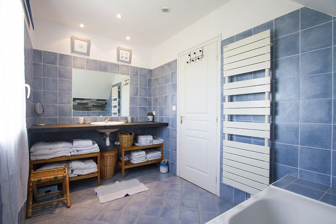 Ein Badezimmer mit einer Badewanne, einem Waschbecken, einem Spiegel und Regalen mit Handtüchern.