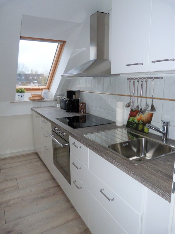 Una cocina moderna con armarios blancos, un lavamanos de acero inoxidable, una placa de inducción negra y una ventana con vistas al exterior.